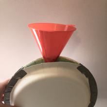 A funnel is inserted in an opening of two plates taped together with duct tape.