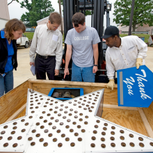 Five people stand around a crate containing a large silver star covered in lights.