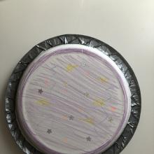 Two plates facing each other taped together with duct tape. The outside of the plate is decorated with stars and purple coloring. 