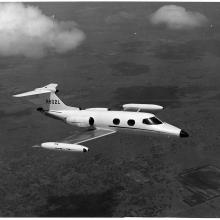 A side view of a small and sleek looking aircraft in flight, as if taken from the window of a nearby aircraft.