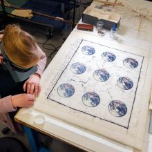 A woman leans over a painting of the Earth conserving it. 