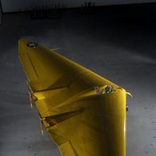 A yellow aircraft that is two wings linked together creating a triangular shape. 