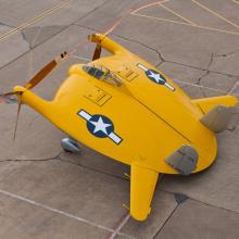 A yellow aircraft shaped like a disk with two propellers emerging from one side, and two wings emerging from the other. 