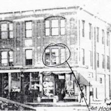 A building on the corner of the street. A circle is drawn around the second floor right hand side window.