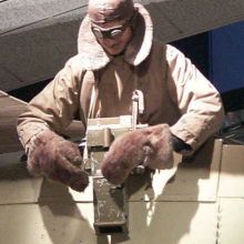 A mannequin leans out of a plane with a camera facing downwards.