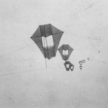 A series of kites fly, they are a polygon shape with a large rectangular opening in the middle. 