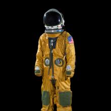 A orange colored full body suit with a helmet attached against a black background.