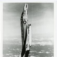 A fighter-style jet in a completely vertical position in the air. The nose of the aircraft points toward the top of the photograph and the tail toward the bottom.