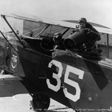 A black and white picture of a plane with a 35 on the side. Two people are in the plane, one pilot and one holding a large camera. 