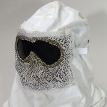 A white hood with goggles propped up for a photograph. The front of the hood has mesh on it, presumably to breathe.