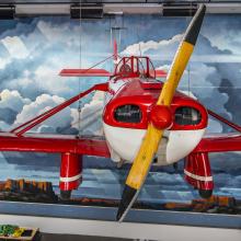 A red and white airplane hang in front of a mural of a Western landscape.