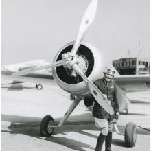 View of the Turner-Laird LTR-14 "Pesco Special" on the ground; pilot Roscoe Turner, in uniform, poses standing behind one blade of propeller at left side of nose of the aircraft.