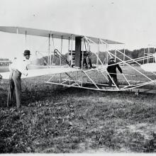 A photo of three men readying the Wright Military Flyer. Two men stand next to its wing, and the other stand between the landing skids.