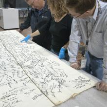 A group of people look at a signed tablecloth. 