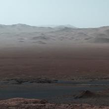 A landscape. In the foreground, is a flat-ish red dusty landscape, in the back is beige hills or mountains.