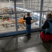 Three visitors look at the X-wing through the windows on the second floor over the Restoration Hangar.