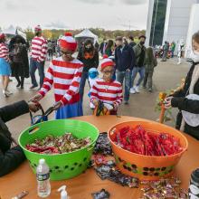 Two kids dressed as Where's Waldo trick or treat outside the Udvar-Hazy Center. There are two large tubs of candy on the tables.