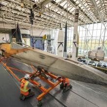 Two workers in a construction vest and helmet adjusts the Star Wars X-wing on its transport device.