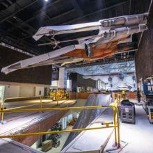 Full size cream and orange X-wing hanging in under-construction space with white plastic coverings on it.