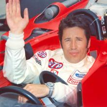 Mario Andretti in the driver's seat of a red race car.