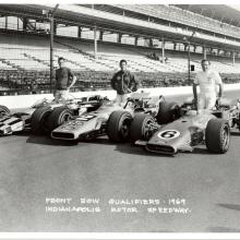 Three men standing behind their Indy 500 race cars.