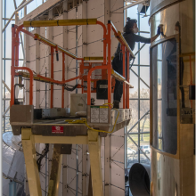 Woman on a lift uses a cloth to clean the shiny exterior of the Skylab space station