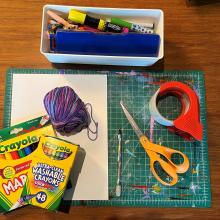 A scissor, tape, markers, yarn, paper, markers and other supplies. 