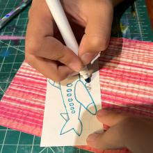 A child's hand draws a plane on a rectangular piece of paper. 