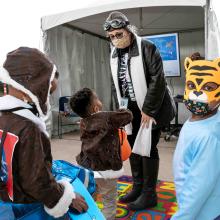 Woman wearing an educator custom gives candy to three young visitors also wearing costumes