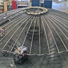 A person lying on top of a large umbrella shaped satellite antenna while cleaning it.