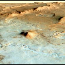 A view of mars surface. Mounds and valleys can be seen. In the forefront of the image the surface is a blueish green color and shifts to brown toward the background of the image.