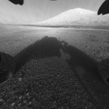 A shadow of a rover is seen in this image. A mountain is in the distance.