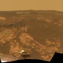 A panoramic view looking out over a hill of the dusty red terrain on Mars.