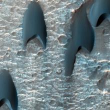 Arrowhead shaped dark splotches cover the cratered surface of Mars.