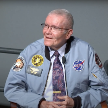 Fred Haise wearing a light blue NASA jacket embroidered with the Apollo 13 patch and a patch for "The Society of Experimental Test Pilots"