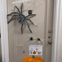 A door with spooky decorations including spiders and cobwebs. Text on the image reads "Family tradition: holiday door decorations."