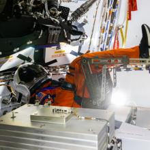 A mannequin wearing an orange spacesuit seated in a spacecraft.