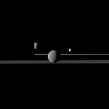 Three moons against a dark background. The moon in the middle appears to be the largest while the moons to the left and right are much smaller looking.