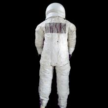 The back of a spacesuit is photographed against a black backdrop