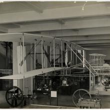 The Wright Flyer on display in an exhibit with other pieces of technology.