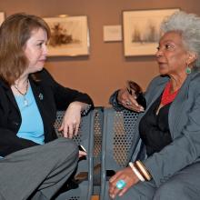 Margaret Weitekamp and Nichelle Nichols sit on a metal bench an talk to one another