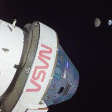 A space capsule is seen at the forefront of the frame while the Earth and Moon is visible in the background.