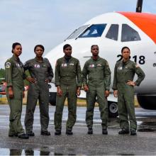 Five black women in flight suits stand in front of an airplane. 