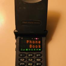 A black flip phone, with a small display screen that read "Phone Book"