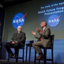 Two men seated on a stage in discussion. The NASA logo is in the background.