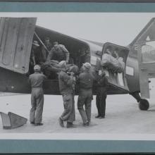 Black and white image of men and women in uniform offloading materials from a plane.