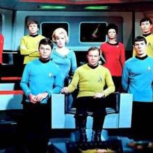 A group of people in primary color uniforms on a spaceship. The people are of different races and genders. 