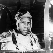 Jesse Leroy Brown looks toward the camera as he sits at the controls of an aircraft.