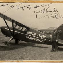 A sepia tone photograph of a small airplane that reads "Kreamy Whip Marshmallows" on the side. A man stands next to it.