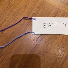 A piece of paper that says "Eat" on it, tied to two strings.